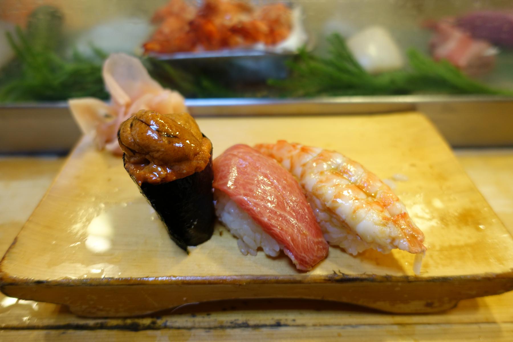 A trio of fresh sushi including uni, fatty tuna, and shrimp on a wooden board.