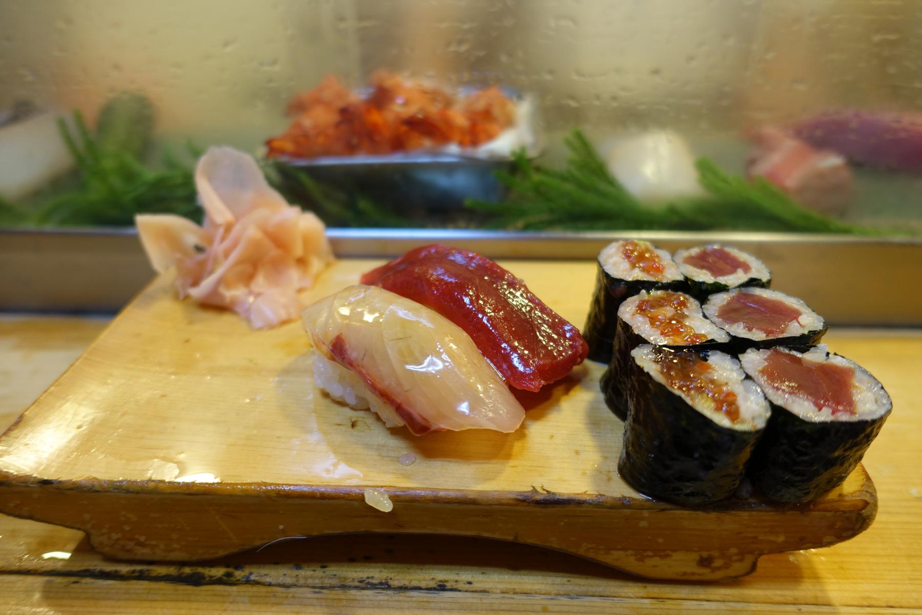 A wooden tray with tuna and white fish nigiri, assorted maki rolls, and pickled ginger.
