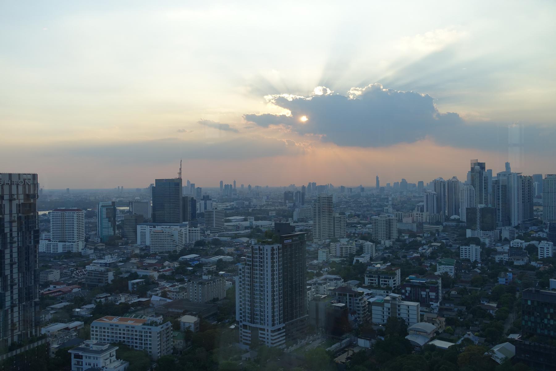 Bangkok cityscape at sunset with sunrays breaking through clouds.