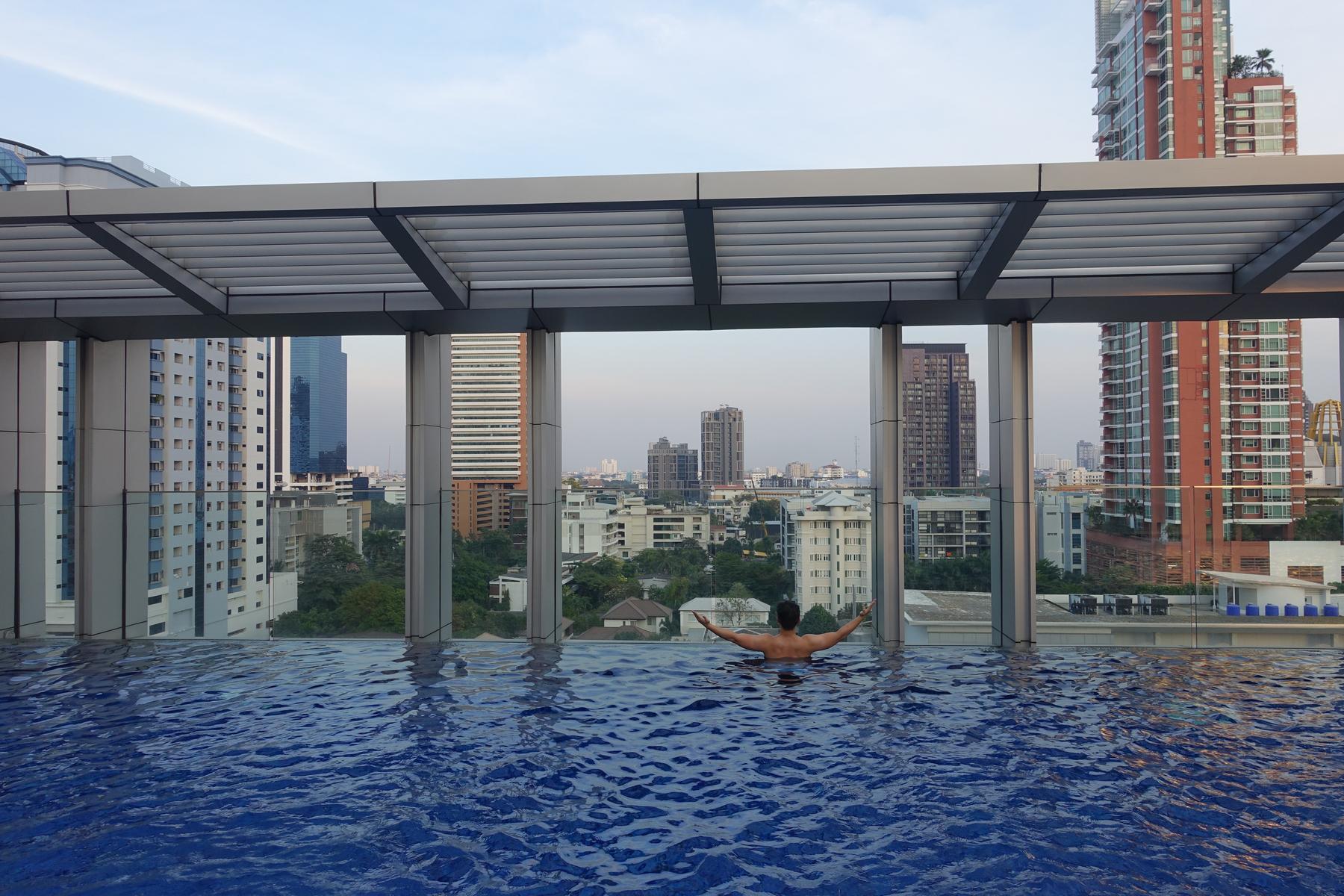Man in a rooftop infinity pool at Bangkok Marriott Sukhumvit overlooking the city.