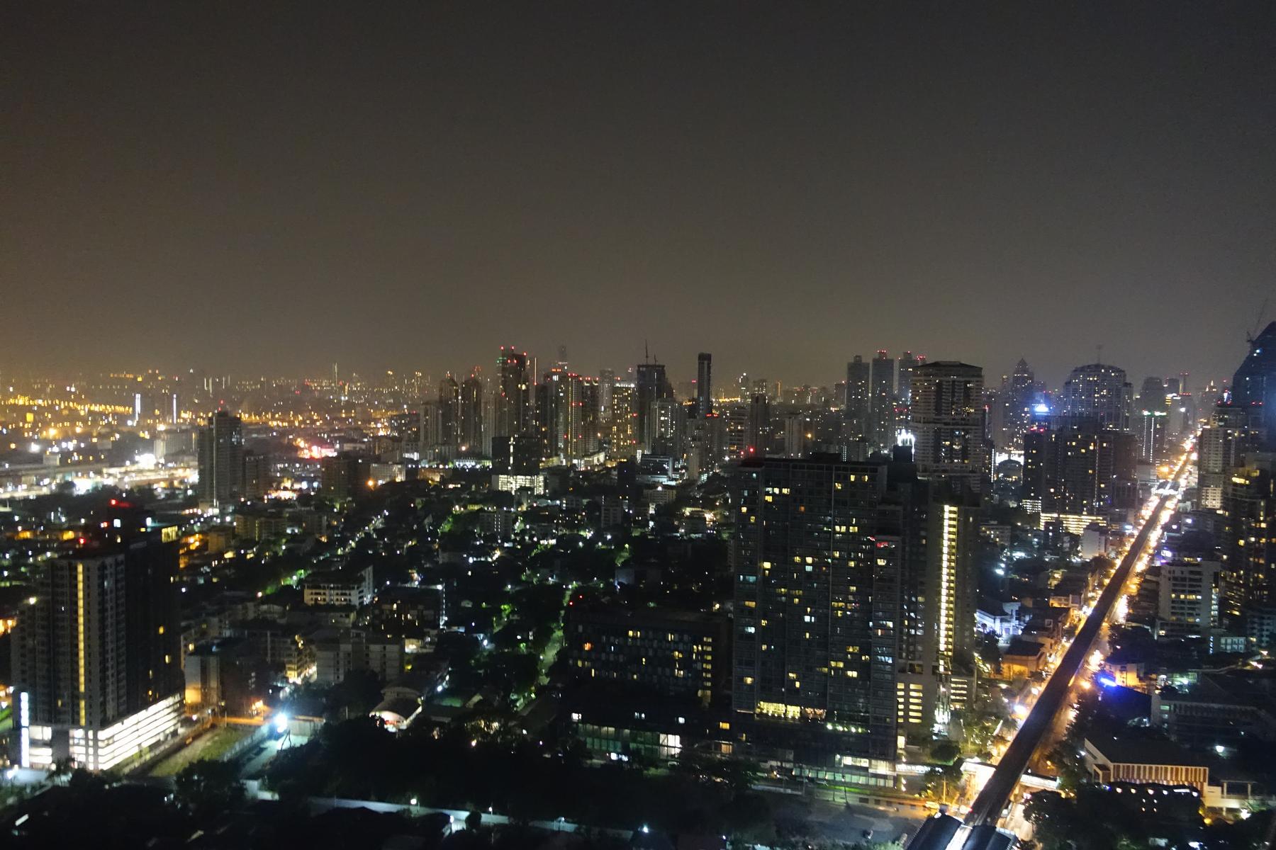 Night view of Bangkok's Thonglor district with illuminated skyscrapers and an elevated train track.