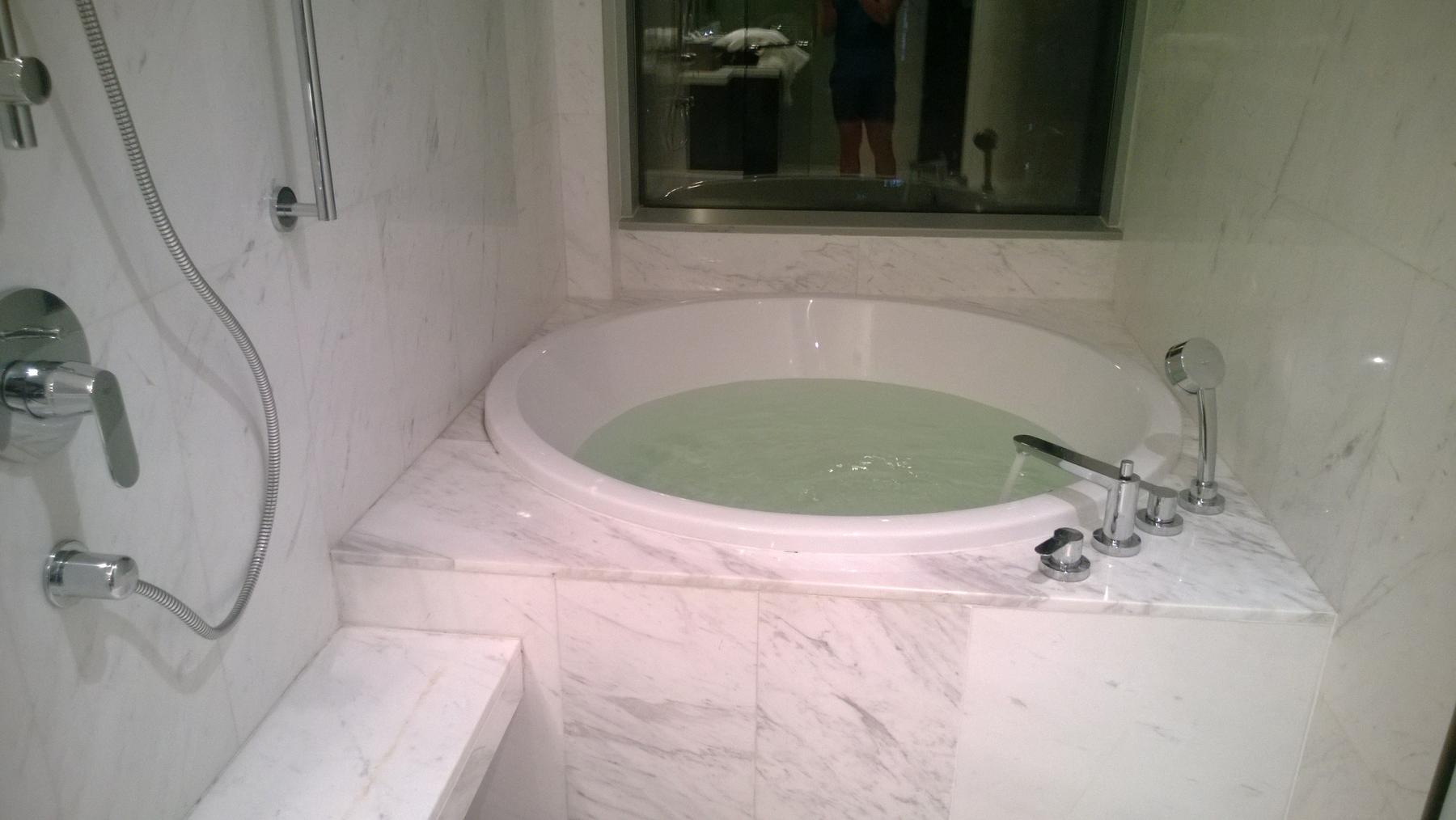 A round bathtub filled with water in a white marble hotel bathroom.