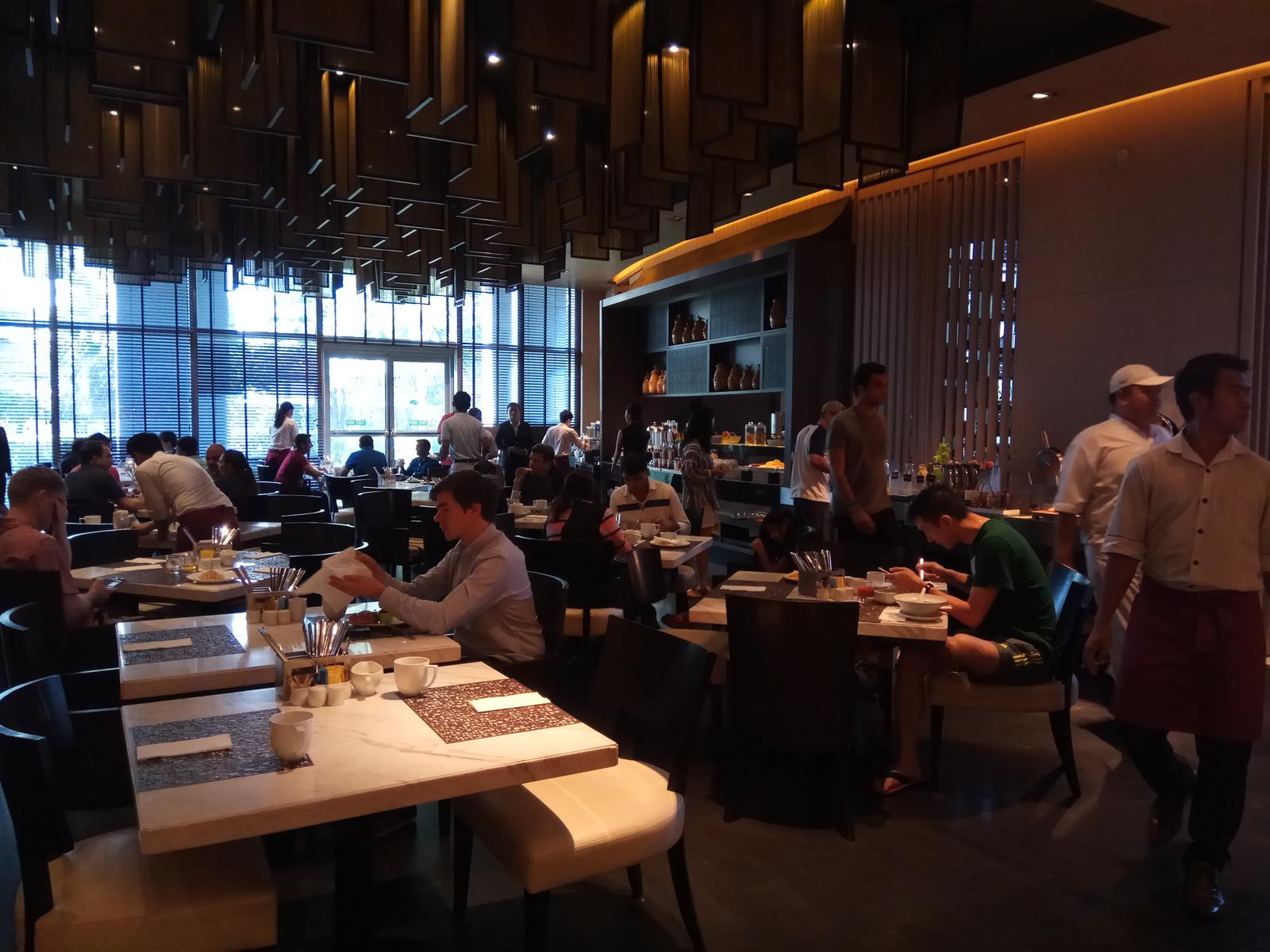 A lively modern hotel restaurant with guests eating and staff serving.