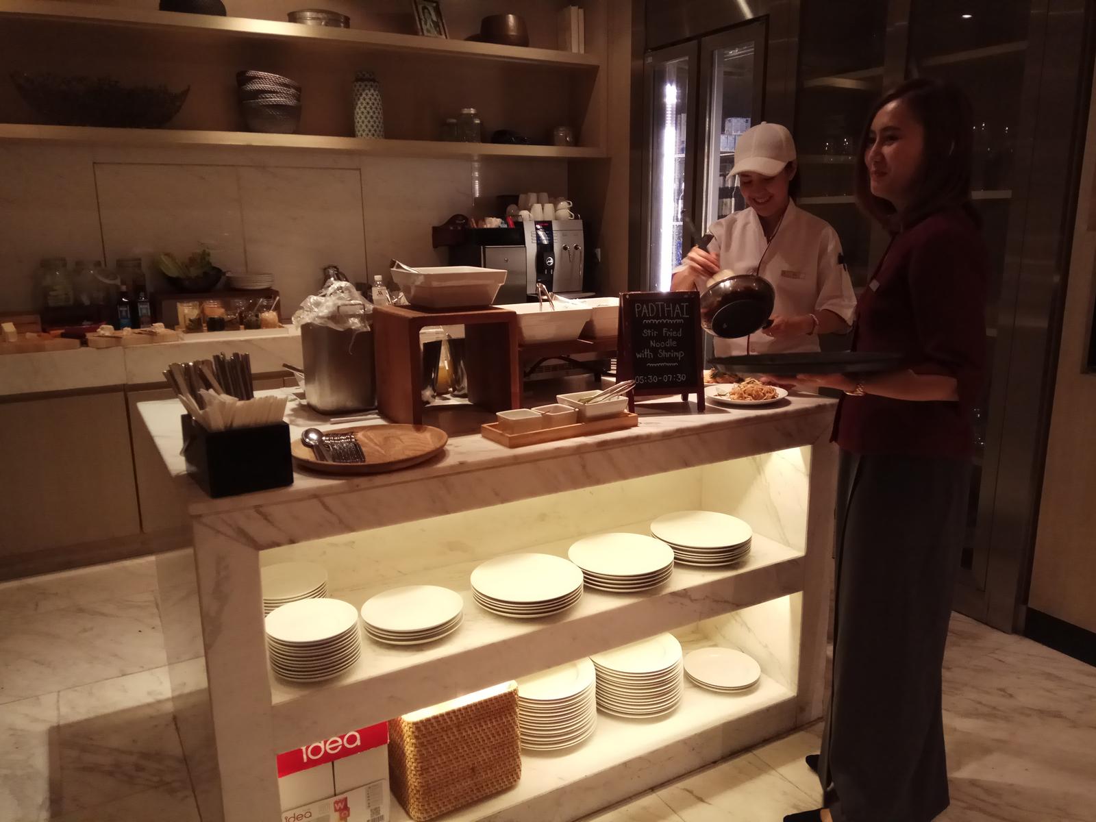 A chef prepares Pad Thai at a live cooking station in a hotel buffet, with a server standing nearby.