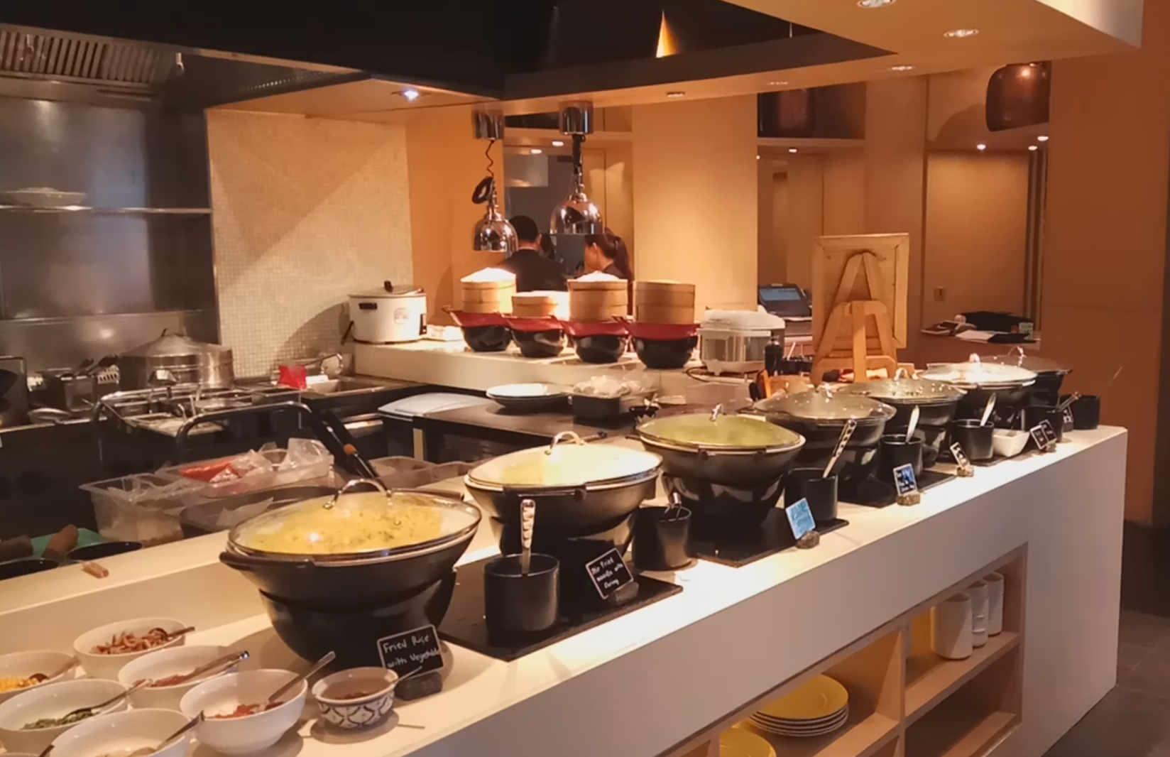A hotel buffet counter featuring hot food warmers, bamboo steamers, and other dishes.