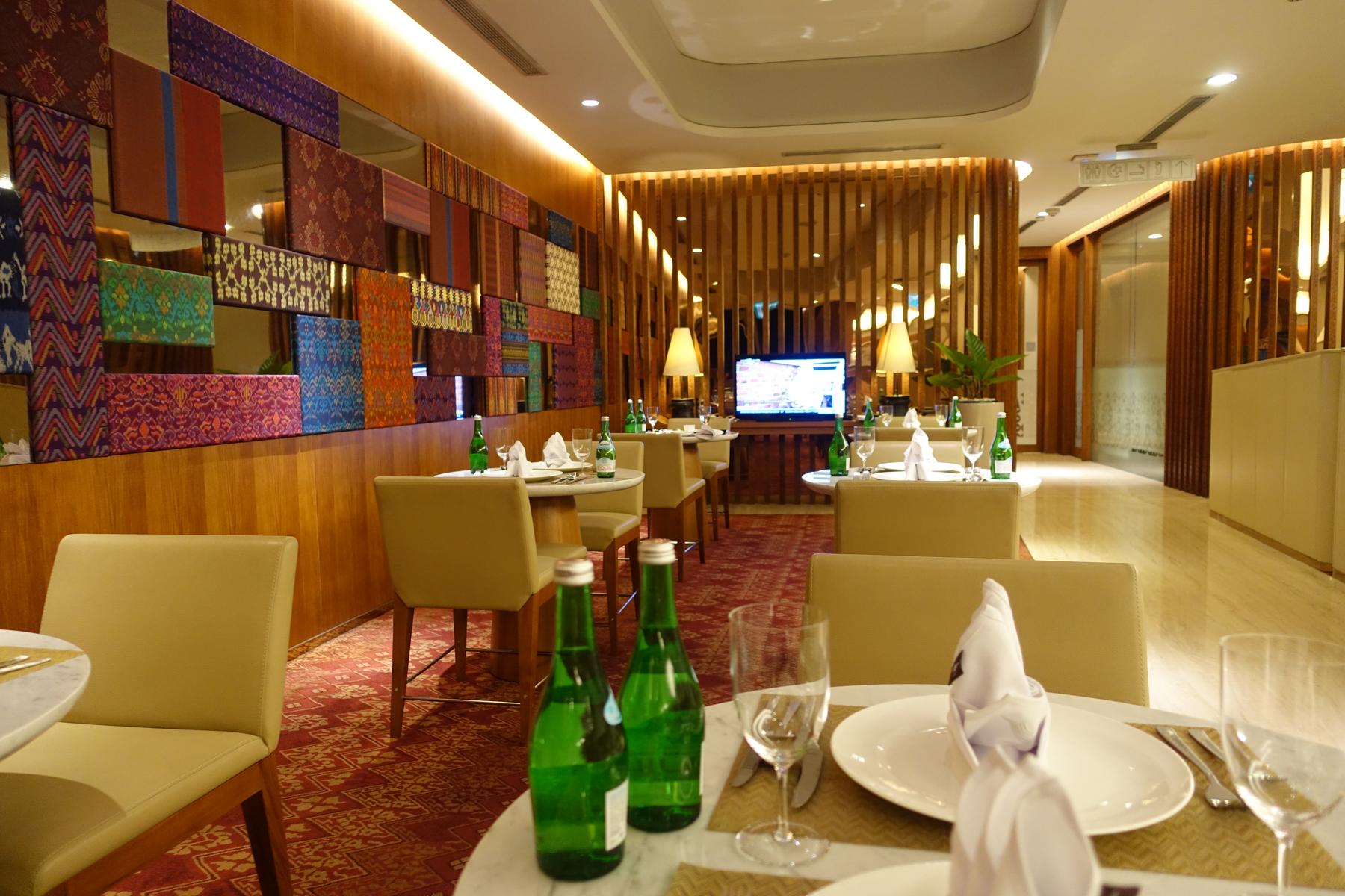 A luxurious first-class lounge dining area with set tables and patterned Indonesian wall art.
