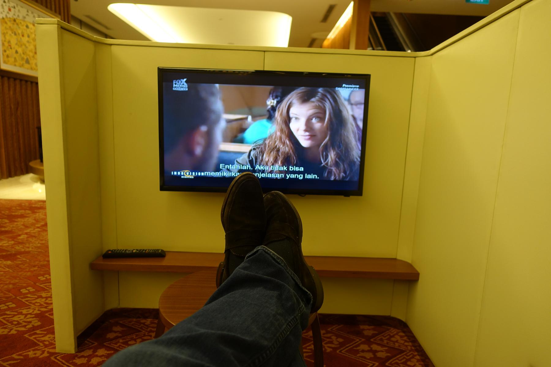 Person's feet up on a table, watching a movie on a TV in a private lounge booth.