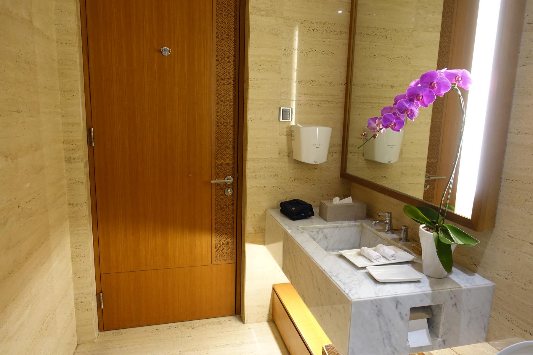 Luxurious restroom with a wooden door, marble sink, mirror, and a vibrant purple orchid plant.