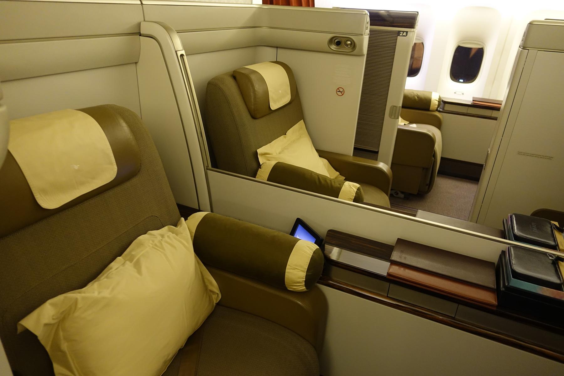 An interior view of a Garuda Indonesia First Class cabin with olive green private suites and cream pillows.
