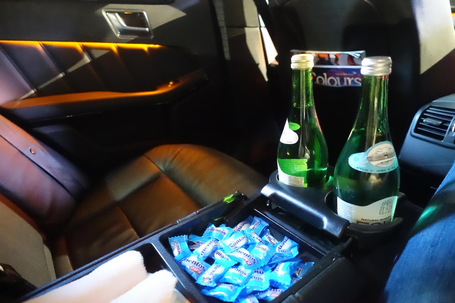 A luxury car interior features two bottles of water and a tray of Mentos candies.