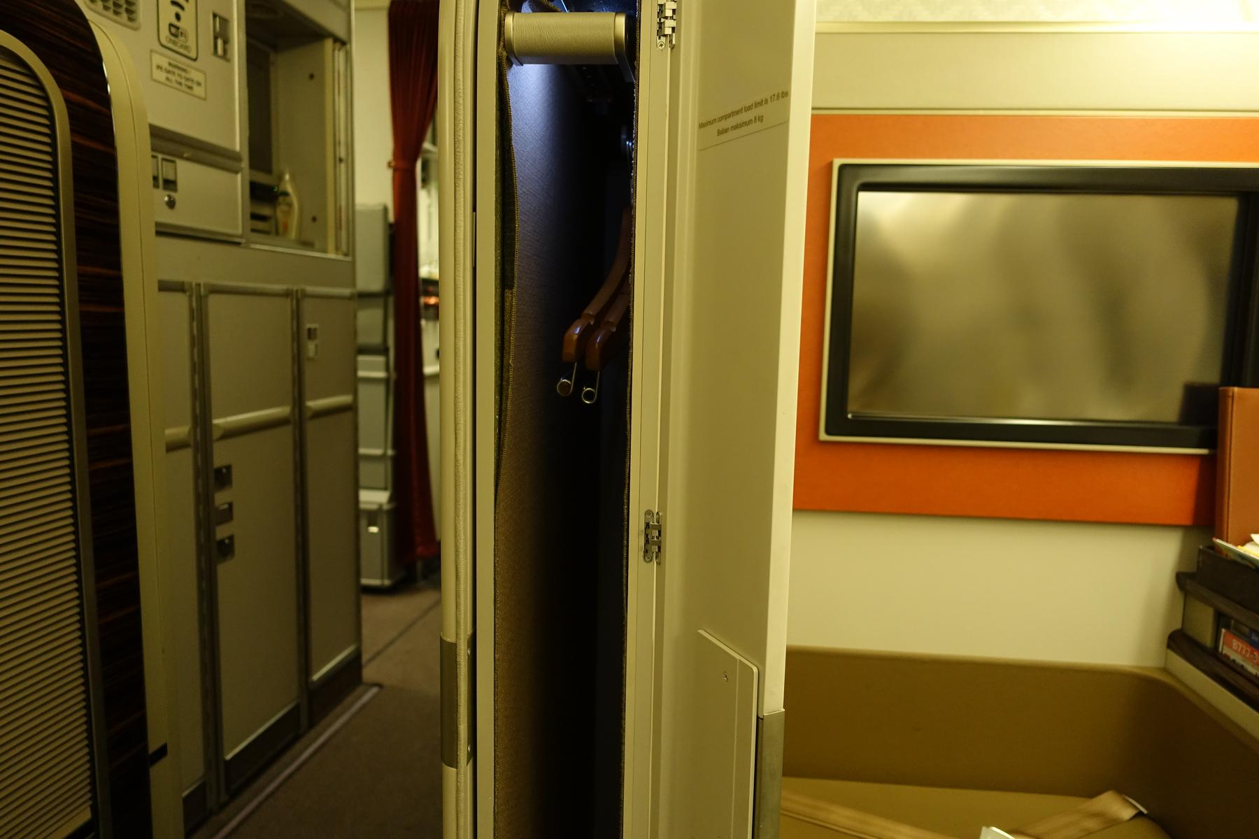 Interior of a Garuda Indonesia First Class cabin showing an open closet, galley, and a private seat with a screen.