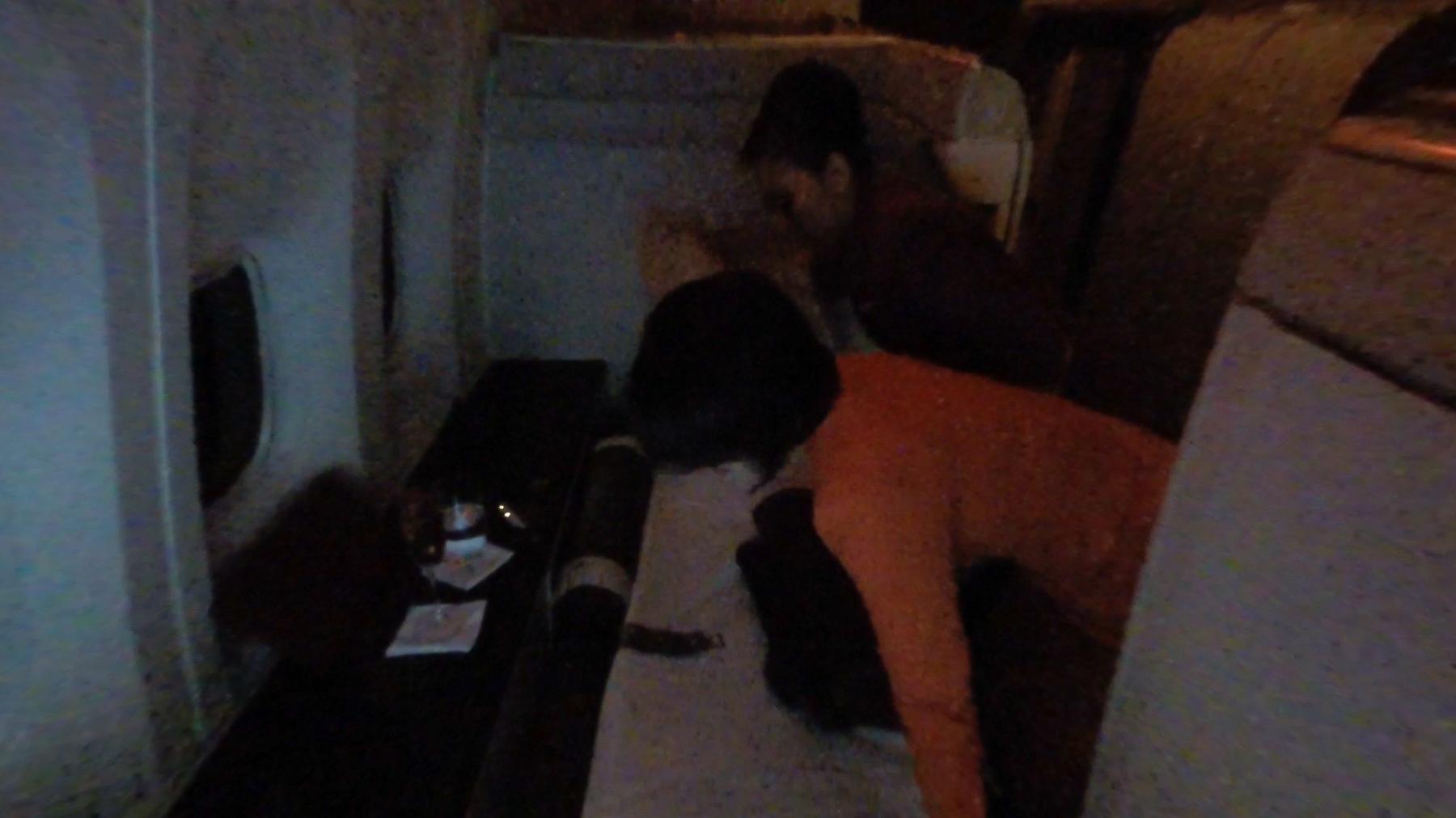 A dark, grainy photo shows two passengers in a Garuda Indonesia First Class cabin, one lying on a flatbed.