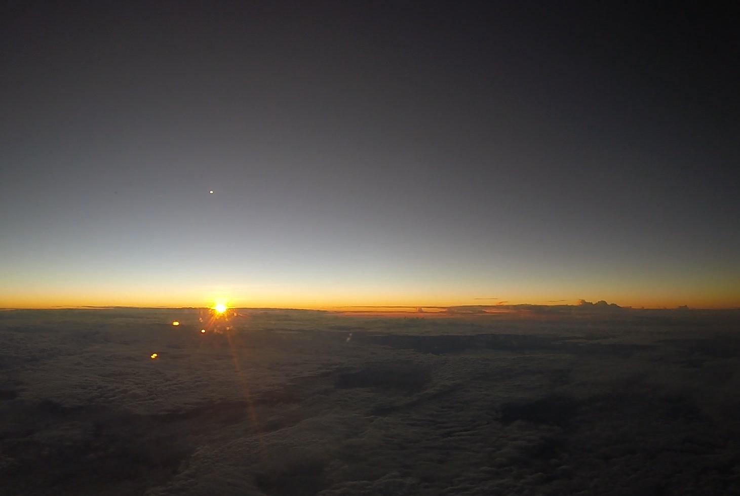 A sunrise viewed from above the clouds with a bright star in the dark sky.