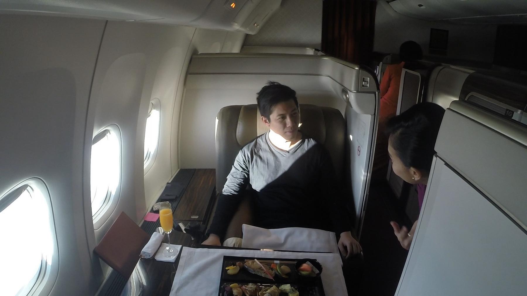 A passenger is served a meal by a flight attendant in a spacious Garuda Indonesia First Class cabin.