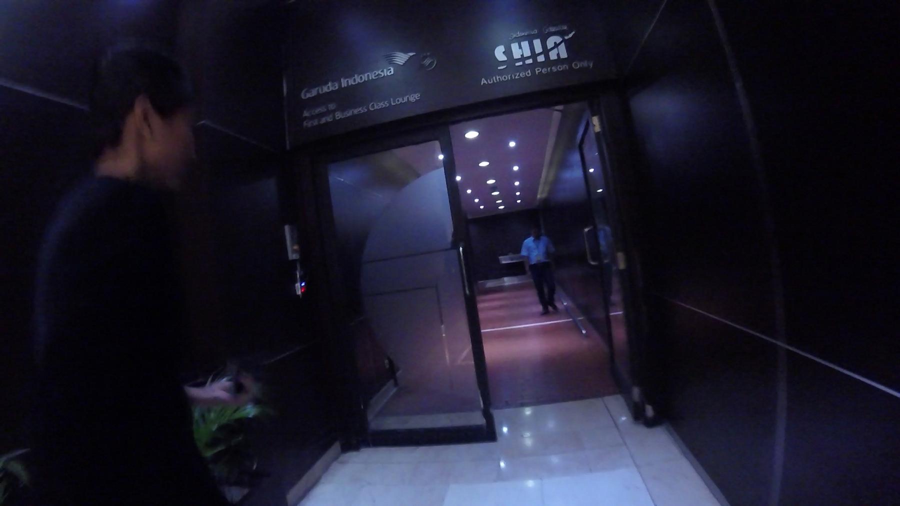 A person enters the Garuda Indonesia First and Business Class Lounge, identified by a sign above the glass doors.