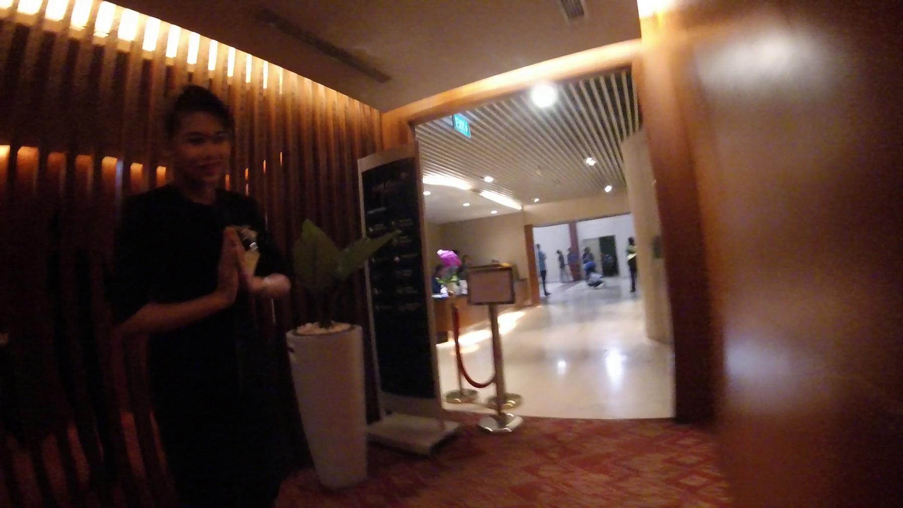 A blurred staff member greets with hands pressed together in a warmly lit lounge.