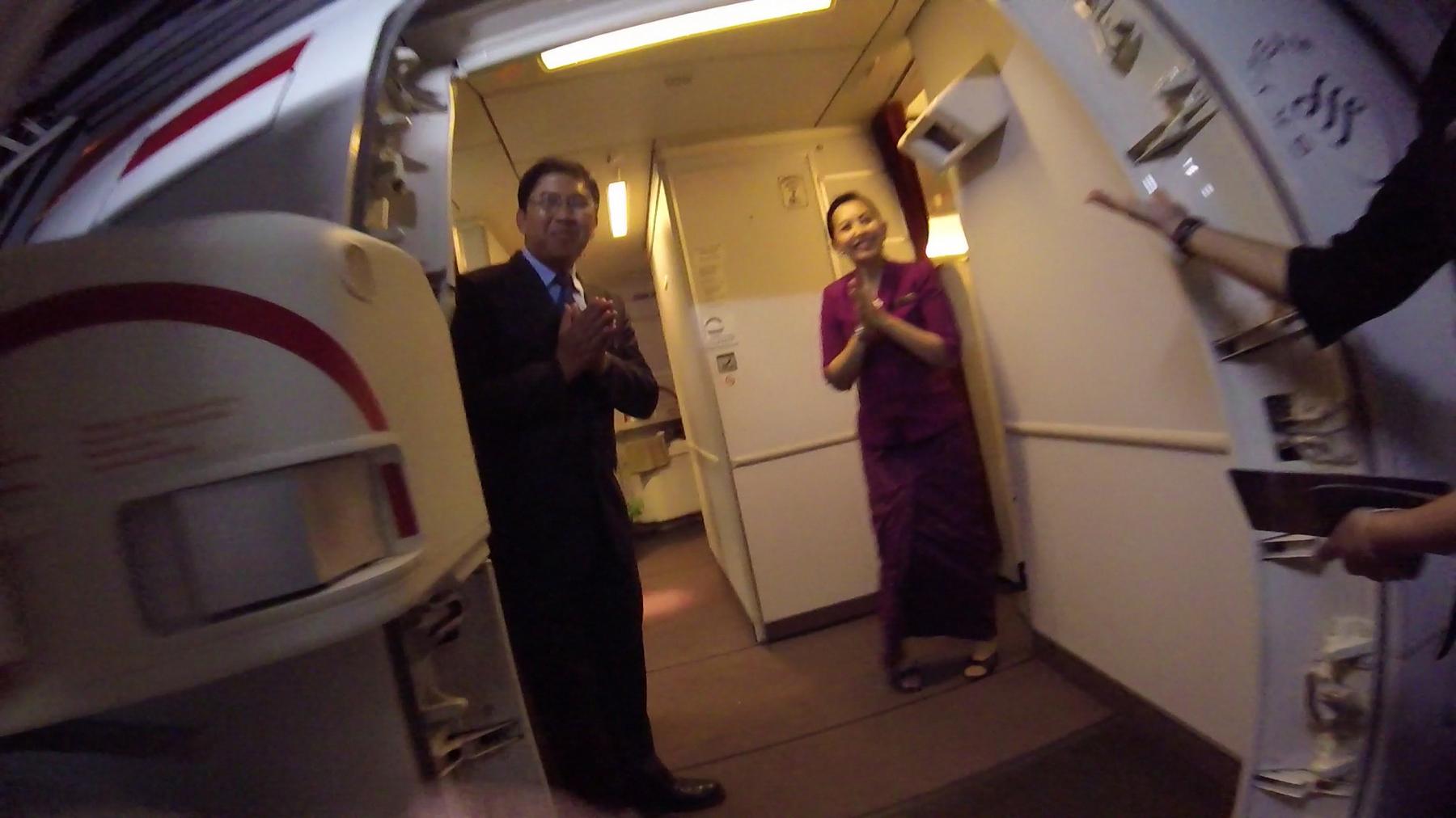 Two smiling Garuda Indonesia flight attendants welcome passengers with hands pressed together inside the aircraft.