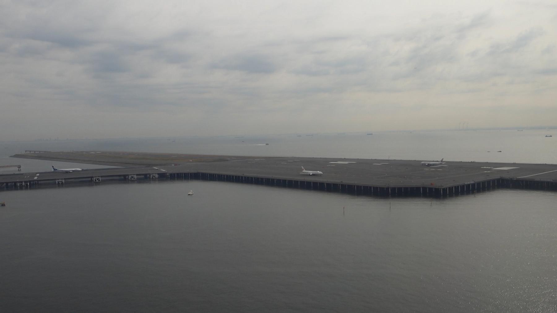 Aerial view of an airport runway extending over the ocean with airplanes on the tarmac.