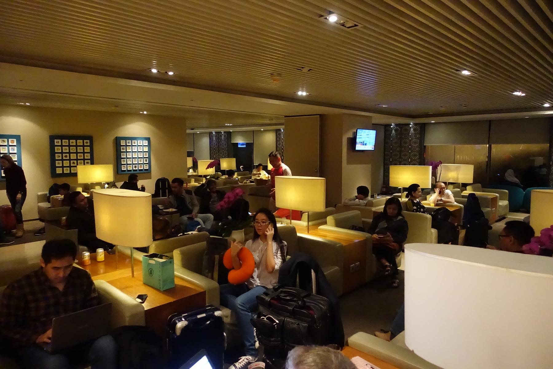 Travelers relax in a warmly lit, comfortable airport lounge with various seating areas.