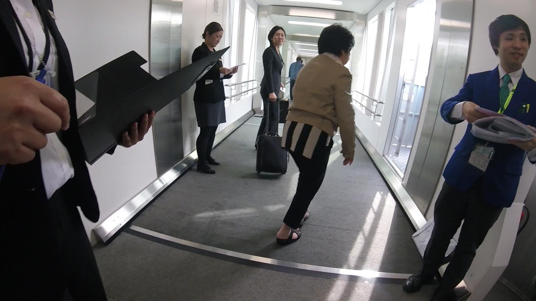 Airport staff and passengers move through a brightly lit jet bridge.