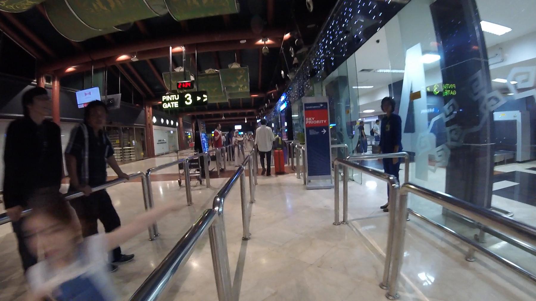 An airport terminal with people walking past signs for Gate 3 and Sky Priority.