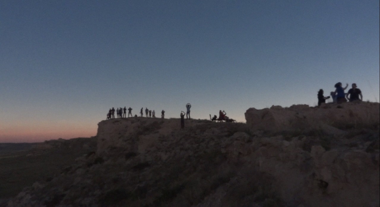 A group of people silhouetted on a rocky hill against a twilight sky during an eclipse.