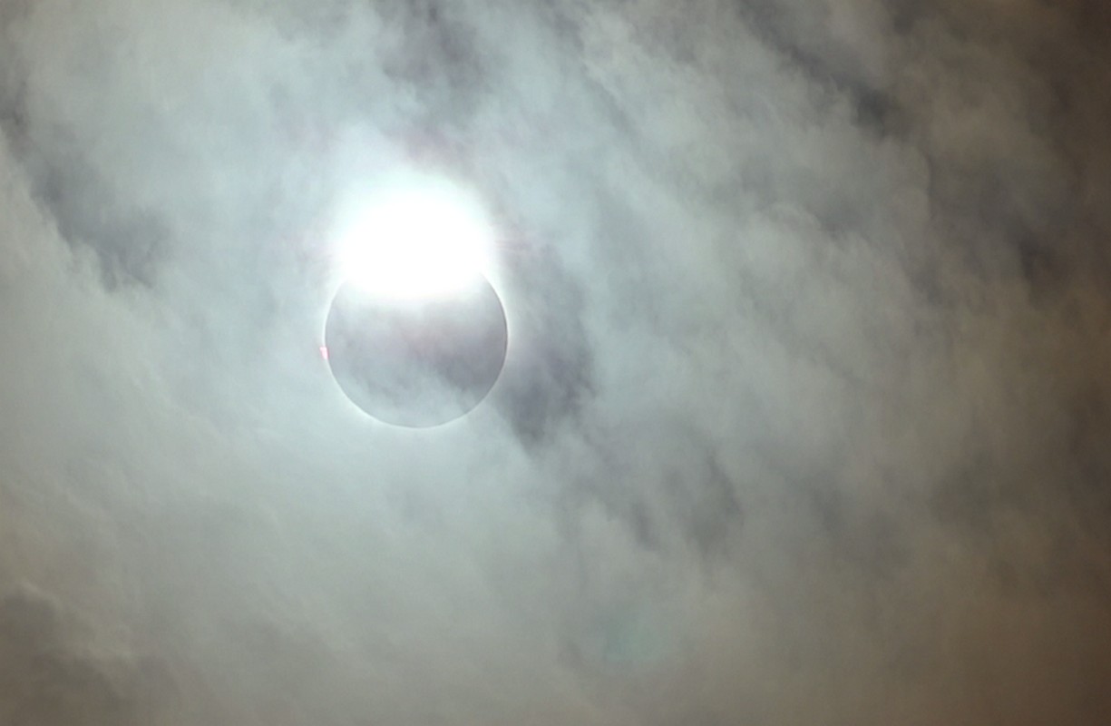 A solar eclipse glows brightly behind hazy clouds.