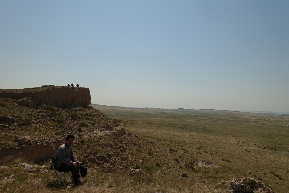 A man sits on a hill overlooking a vast Nebraska plain, with others on a distant bluff.