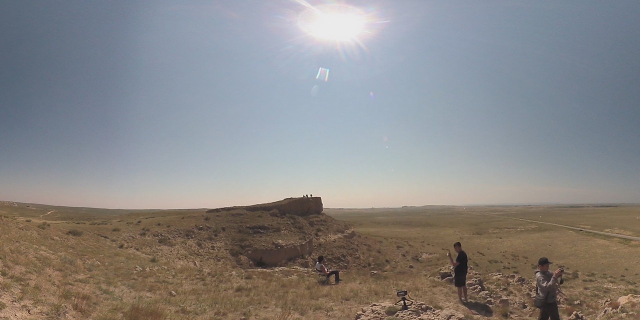 Family gathers in a wide, sunny Nebraska landscape to watch the Great American Eclipse.