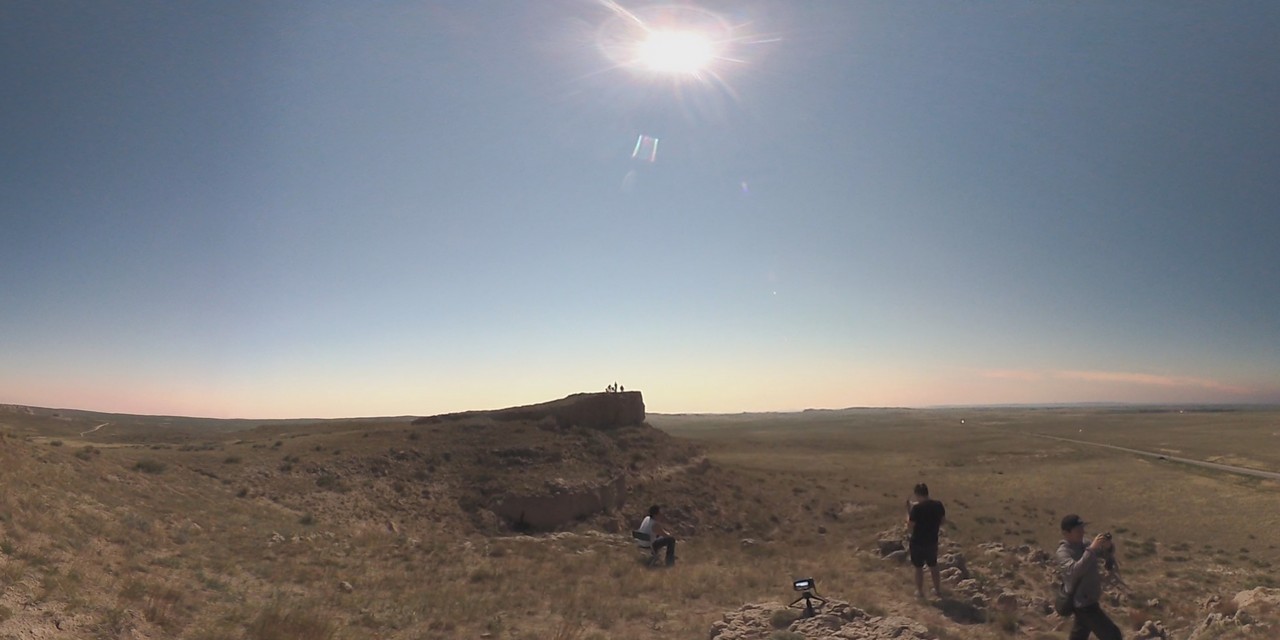 People watch the bright sun from a wide Nebraska landscape during an eclipse.