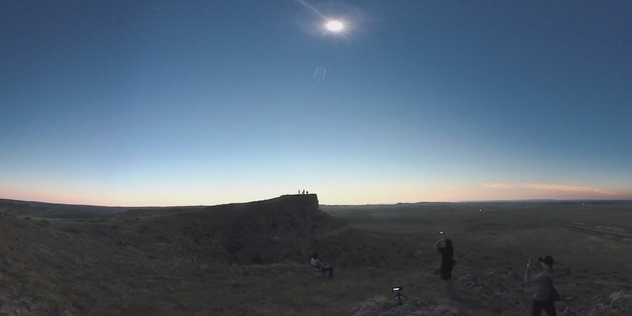 A total solar eclipse shines brightly in the sky above people watching from a vast Nebraska landscape.