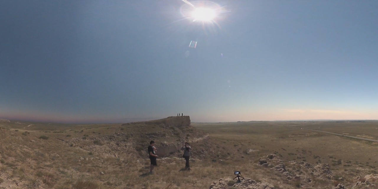 A wide view of people on a bluff and hill in a sunny, grassy Nebraska landscape.