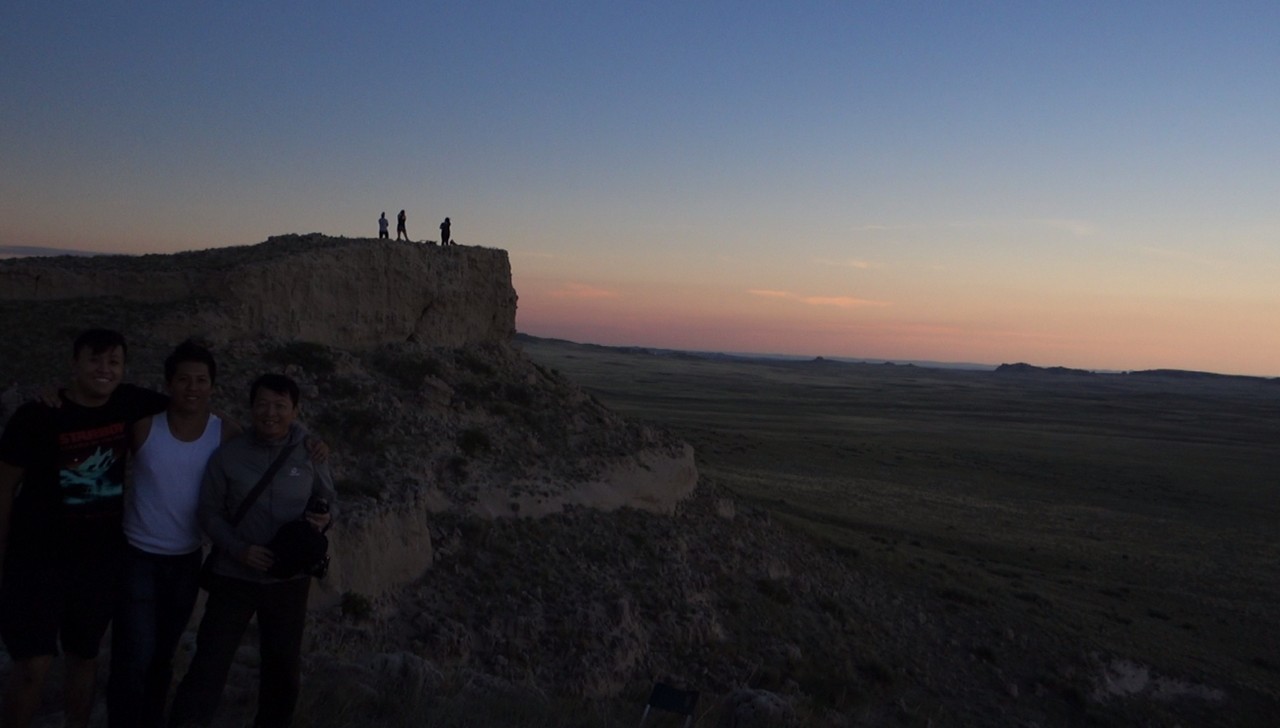 Three family members pose on a rocky hill in Nebraska as others watch the Great American Eclipse under a colorful twilight sky.
