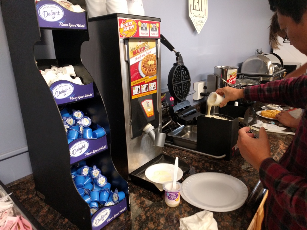A person pours batter into a waffle maker at a breakfast buffet.