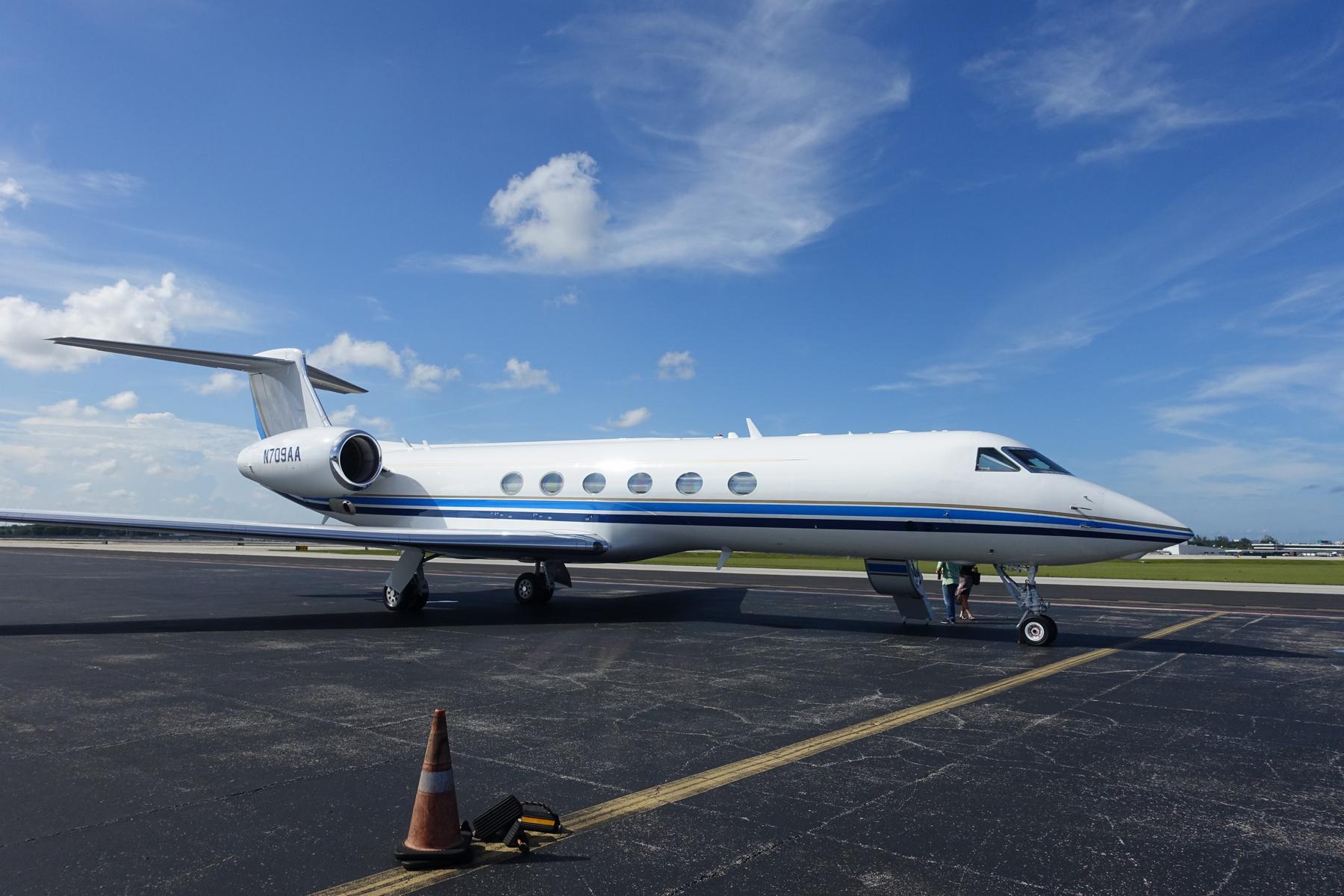 A white Gulfstream 500 private jet sits on an airport tarmac under a blue sky.