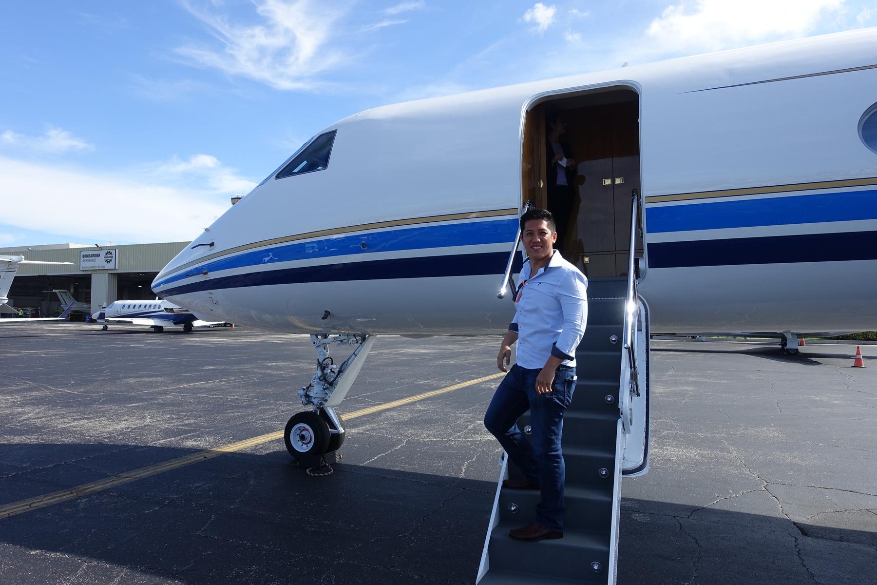 Man smiles while standing on the steps of a Gulfstream 500 private jet on a sunny tarmac.