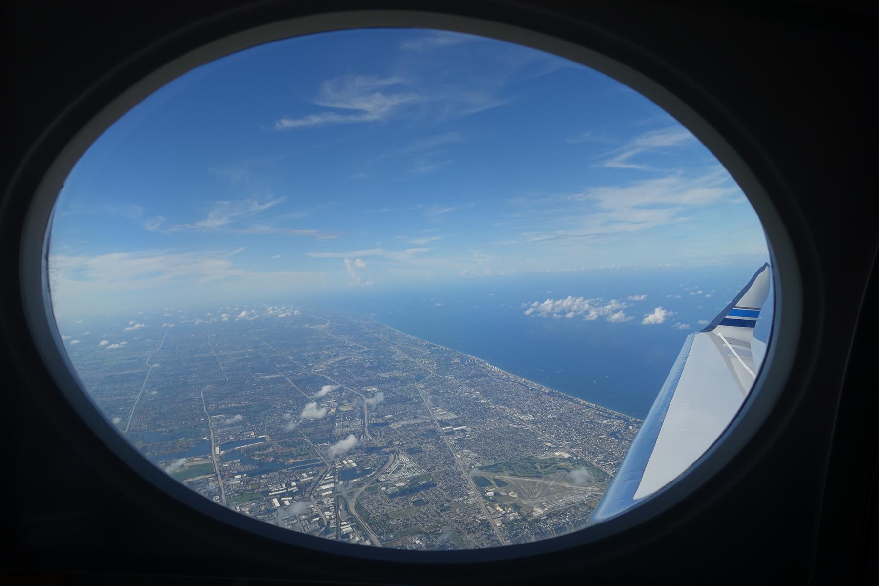 Aerial view from a private jet window showing the Florida coastline, ocean, and part of the plane's wing.