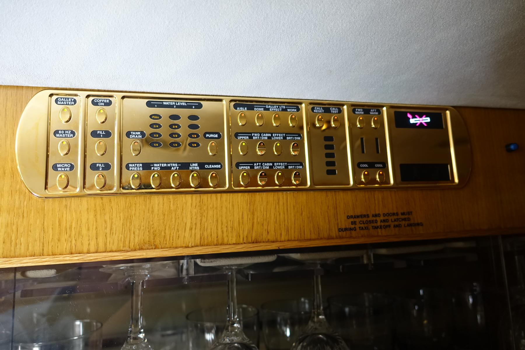 Gold control panel for galley and cabin functions inside a private jet.