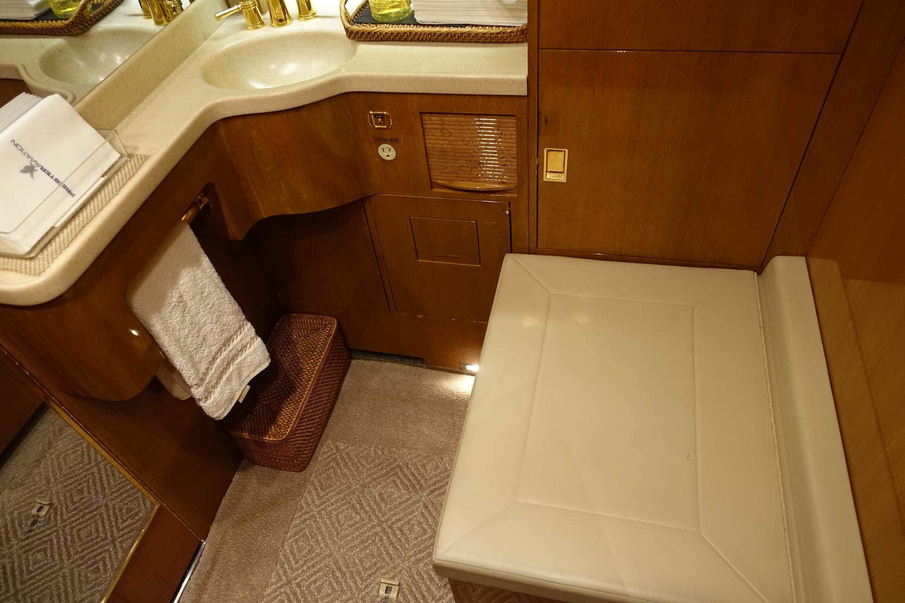 An elegant private jet lavatory with wood paneling, dual sinks, and a toilet with a cream padded seat.