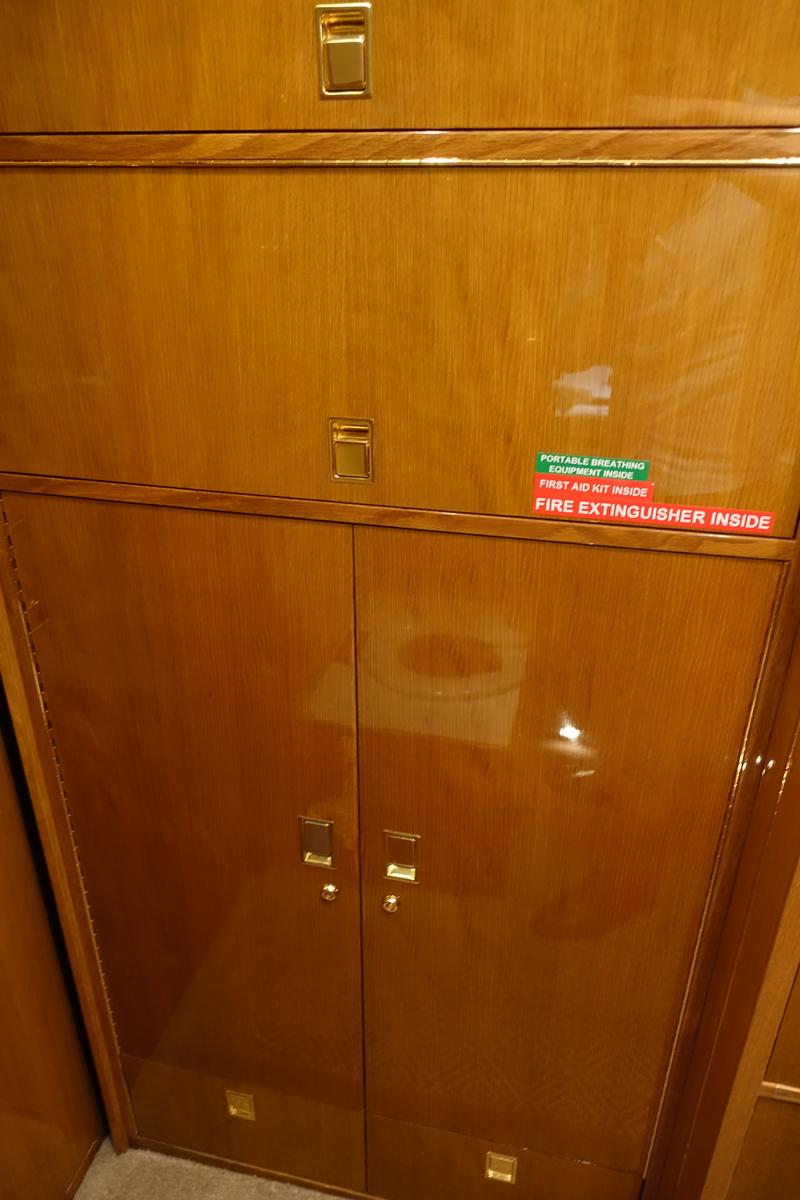 Private jet interior showing polished wood cabinets with gold handles and emergency equipment labels.
