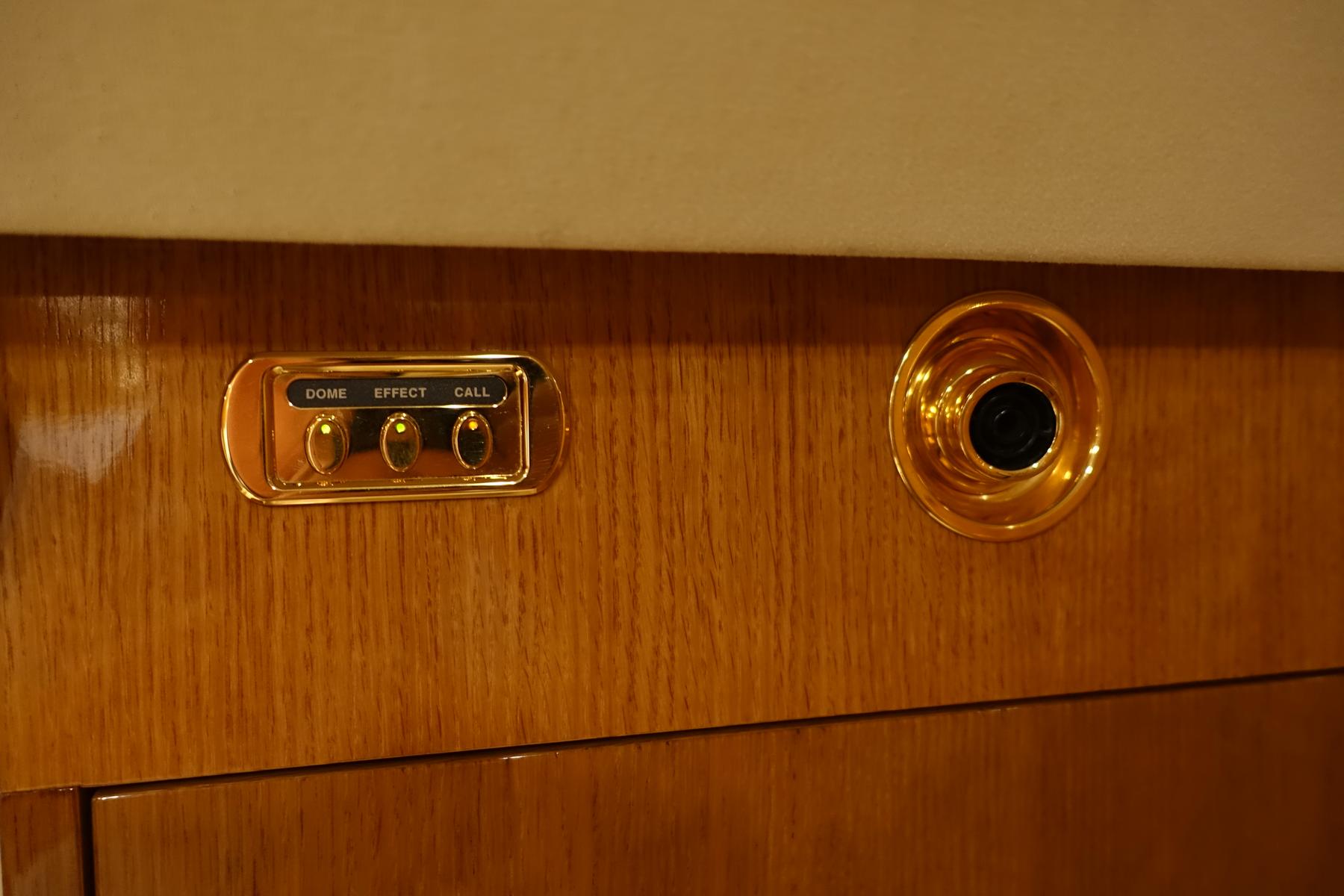 Gold control panel with light and call buttons and a speaker on a polished wood private jet interior.