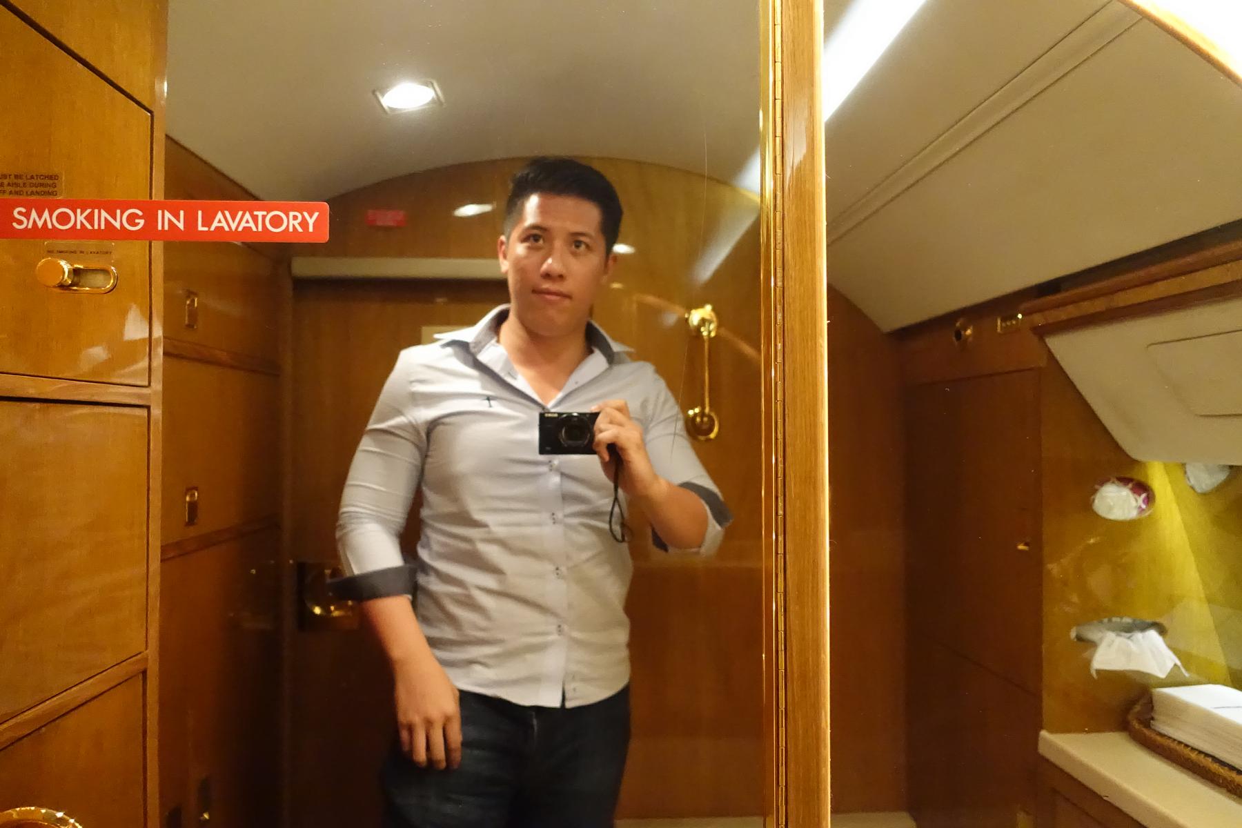 A man takes a mirror selfie in a private jet lavatory with a "NO SMOKING" sign visible.