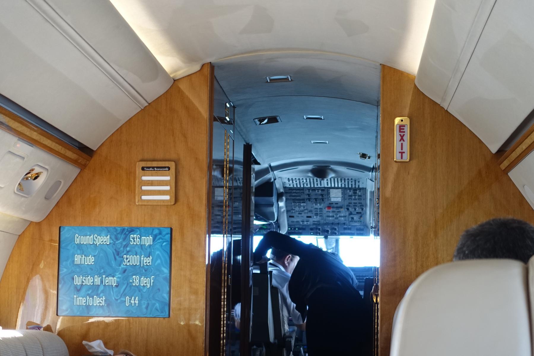 View from a private jet cabin looking into the cockpit, with a screen displaying flight information.