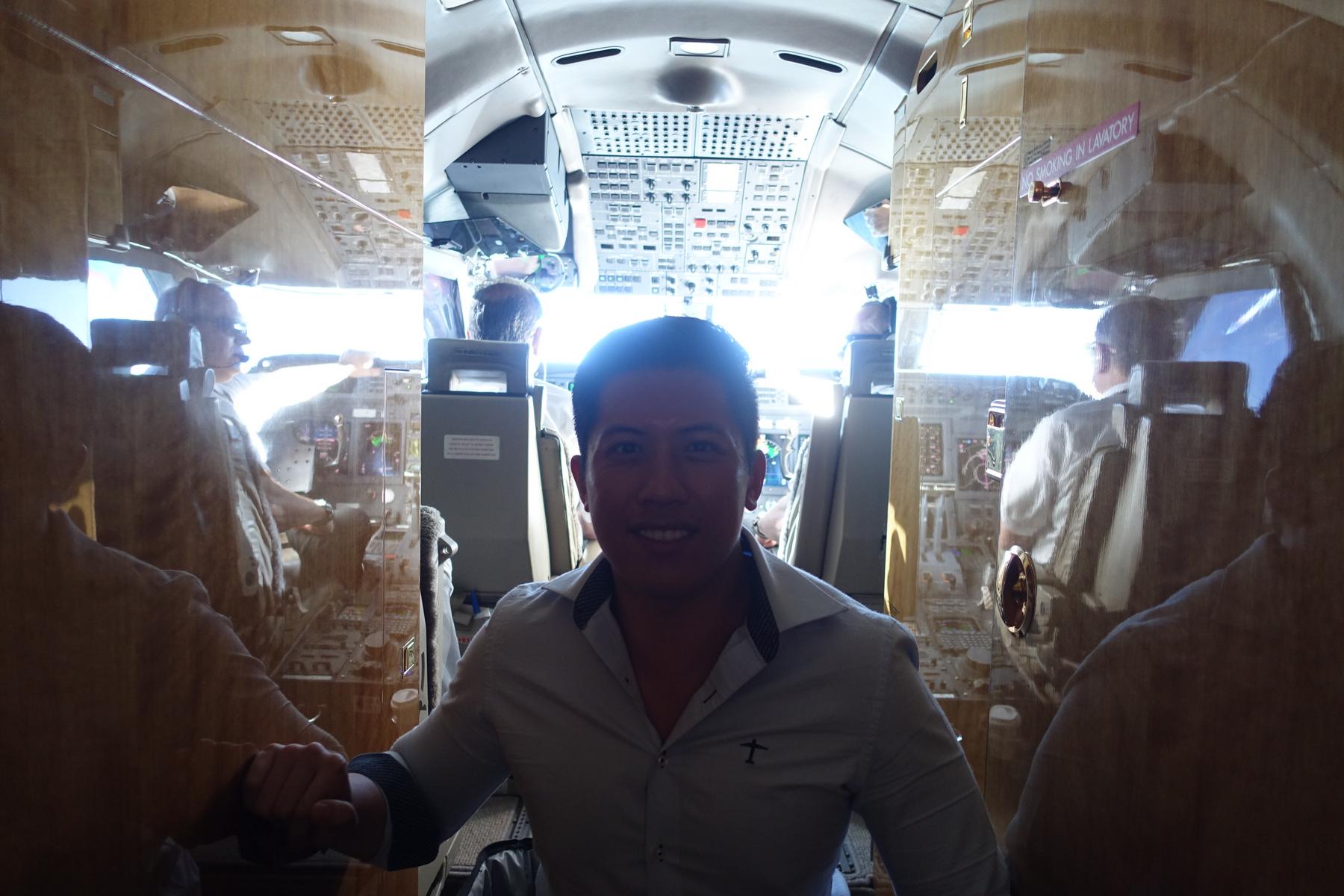 A man smiles from the cabin of a Gulfstream G5 private jet, with the cockpit and pilots visible behind him.