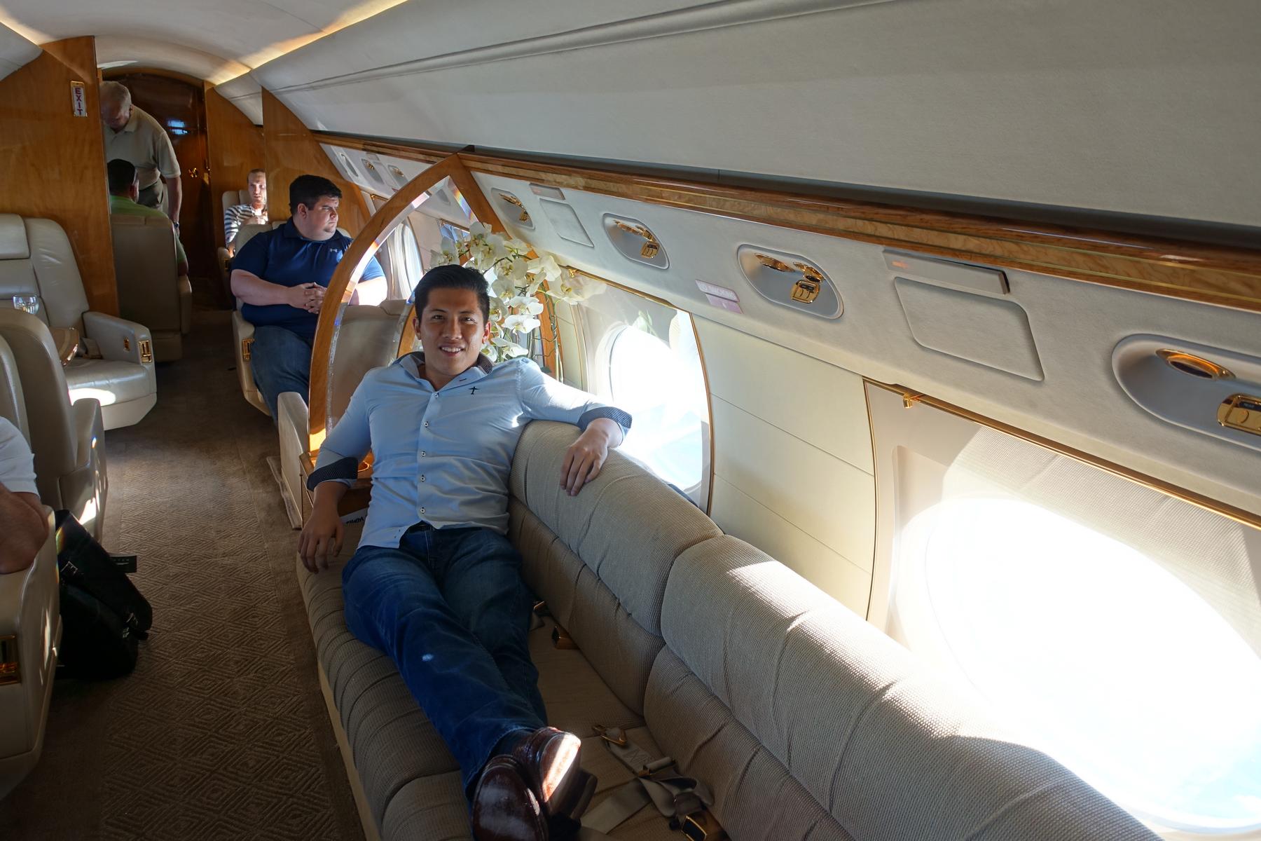 A smiling man relaxes on a plush sofa inside a luxurious Gulfstream G5 private jet.