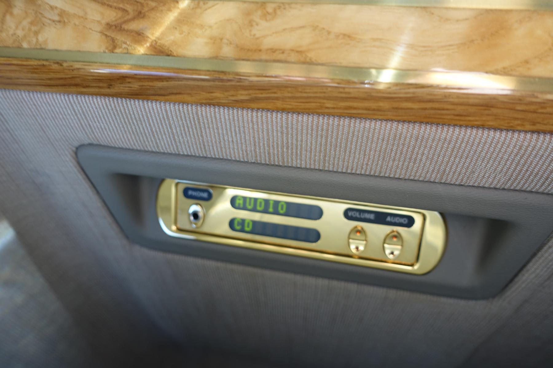 A gold-finished entertainment control panel with a phone jack, audio, and CD displays inside a private jet cabin.