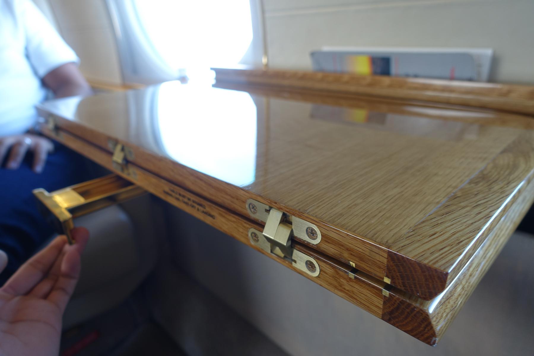 A hand adjusts the extended, polished wooden tray table inside a private jet.