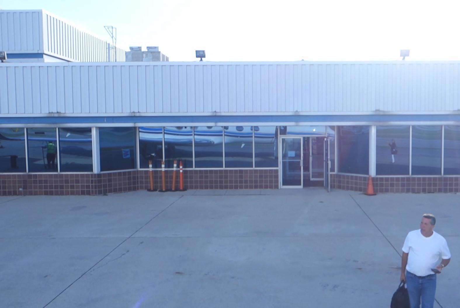 A man walks on the tarmac outside a terminal building, its windows reflecting a private jet.