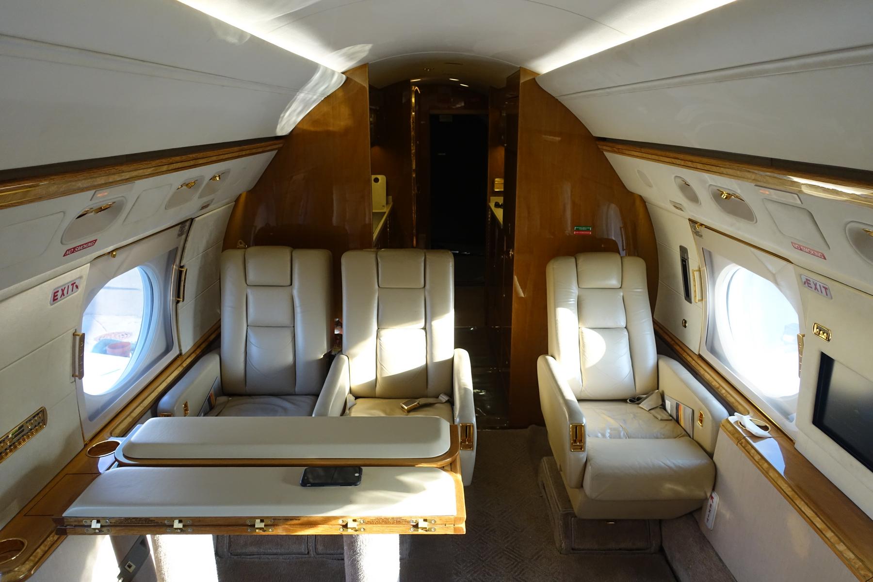 Luxurious interior of a Gulfstream 500 private jet cabin with cream leather seats and wood paneling.
