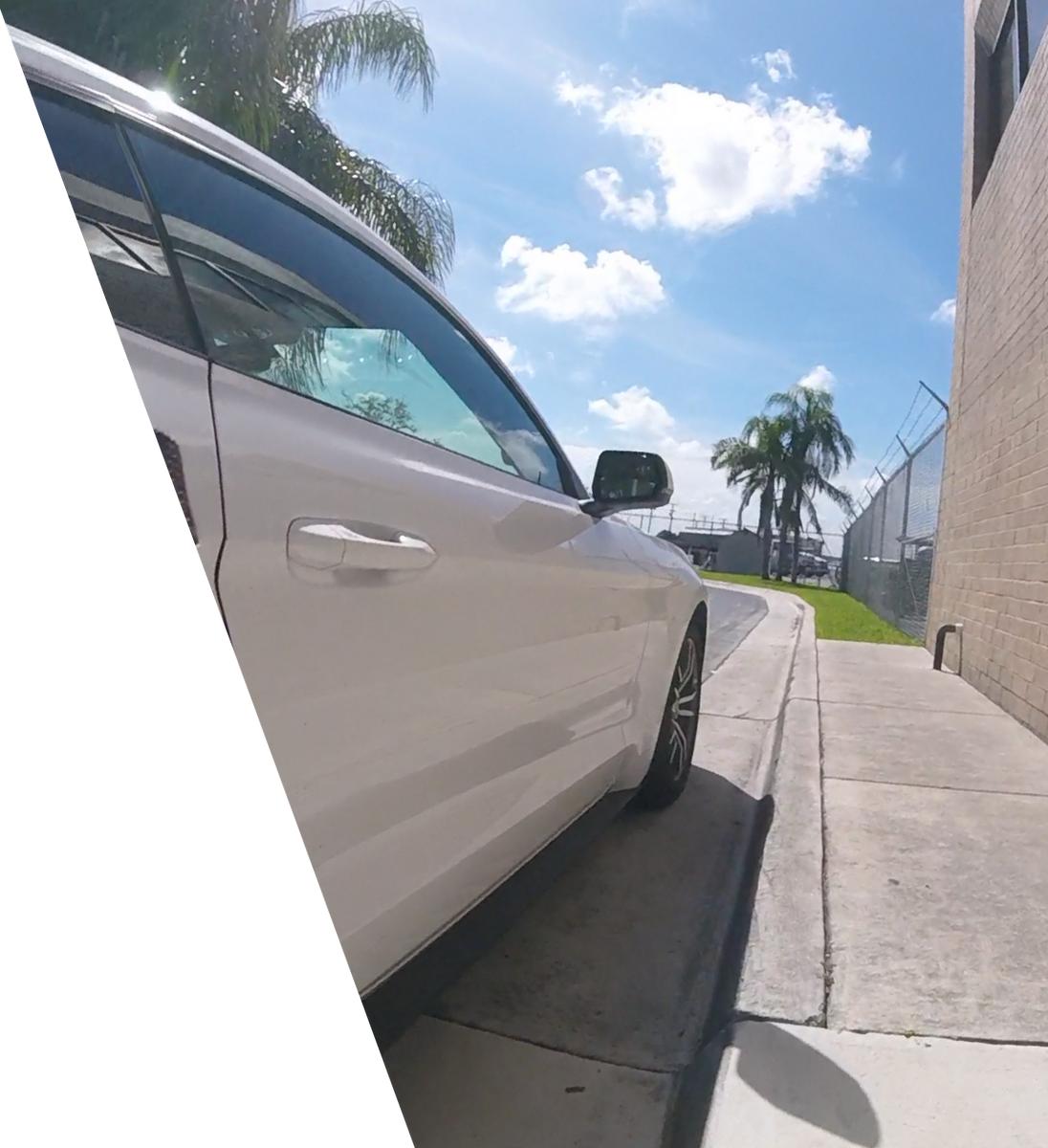 A white car parked outdoors on a sunny day with palm trees and a blue sky.